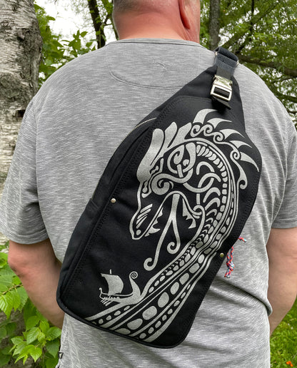 Close Up Photo of Dock 5’s hand-crafted Viking Dragon Canvas Sling Bag in black is being worn by a man standing near the shoreline of Park Point