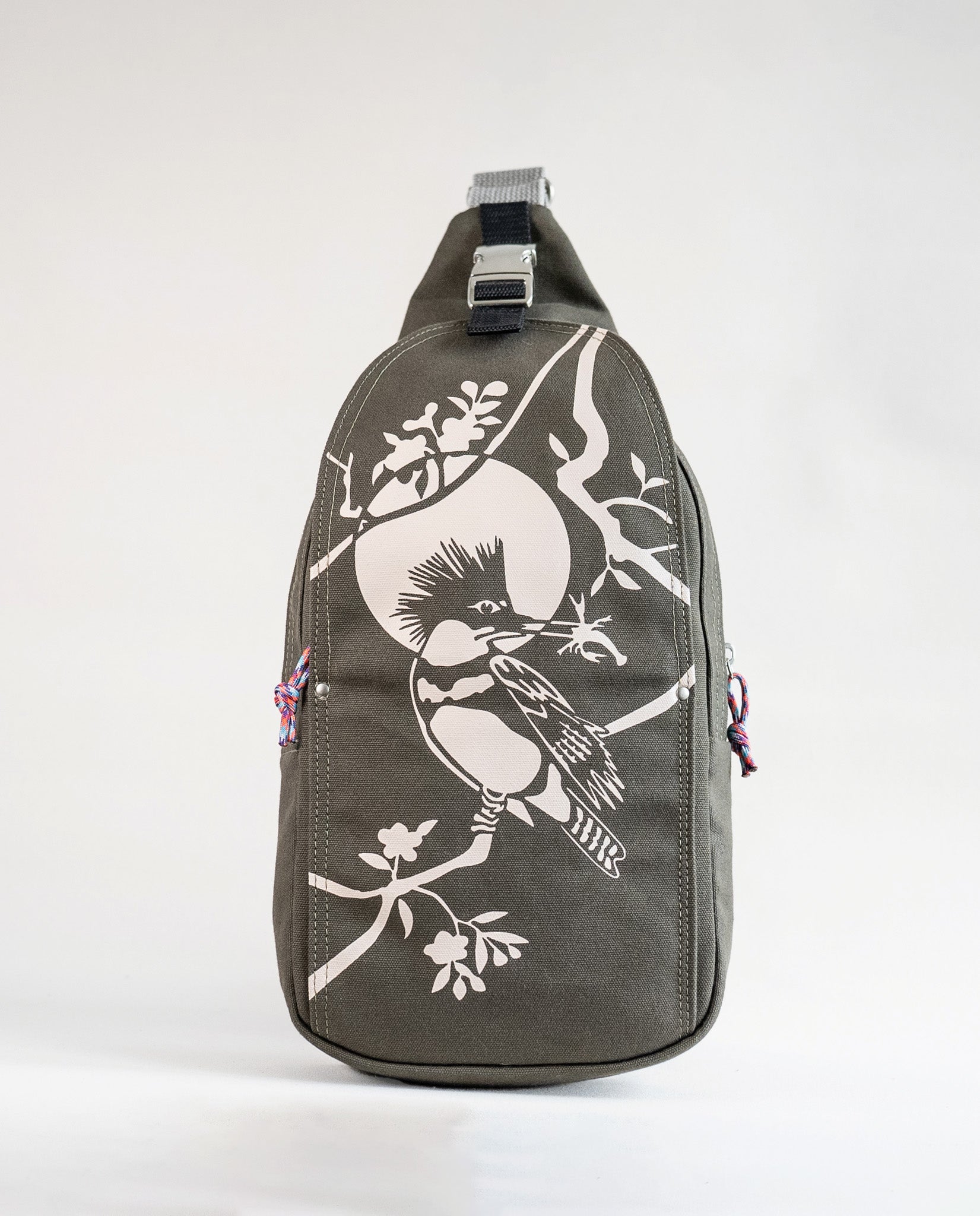 Front exterior of Dock 5’s Kingfisher Canvas Sling Bag in olive featuring art from owner Natalija Walbridge